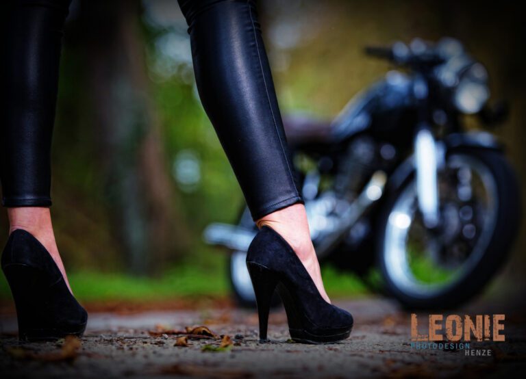 Das Foto zeigt im Vordergrund nur die Beine einer Frau in High Heels, im Hintergrund ist verschwommen ein Motorrad zu sehen.