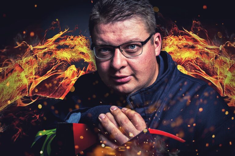 Das Foto zeigt einen Feuerwehrmann, in den Hintergrund ist Feuer montiert, er hat eine Axt in der Hand.