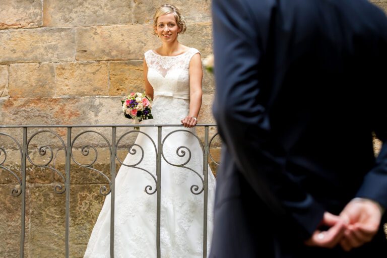 Das Foto zeigt ein junges Ehepaar sie schaut ihn an, er ist nichg ganz zu sehen, steht mit dem Rücken zu Kamera und hält etwas hinter seinem Rücken.