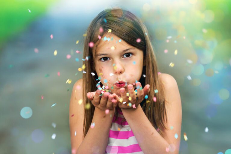 Das Foto zeigt ein Kind, welches Konfetti aus seiner Hand pustet