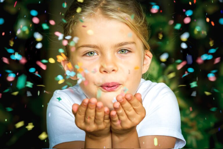 Das Foto zeigt ein Kind, welches Konfetti aus seiner Hand pustet