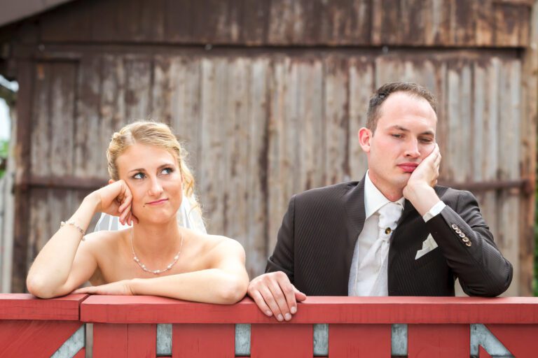 Das Foto zeigt ein junges Ehepaar die gelangweilt auf einem Zaun lehnen.