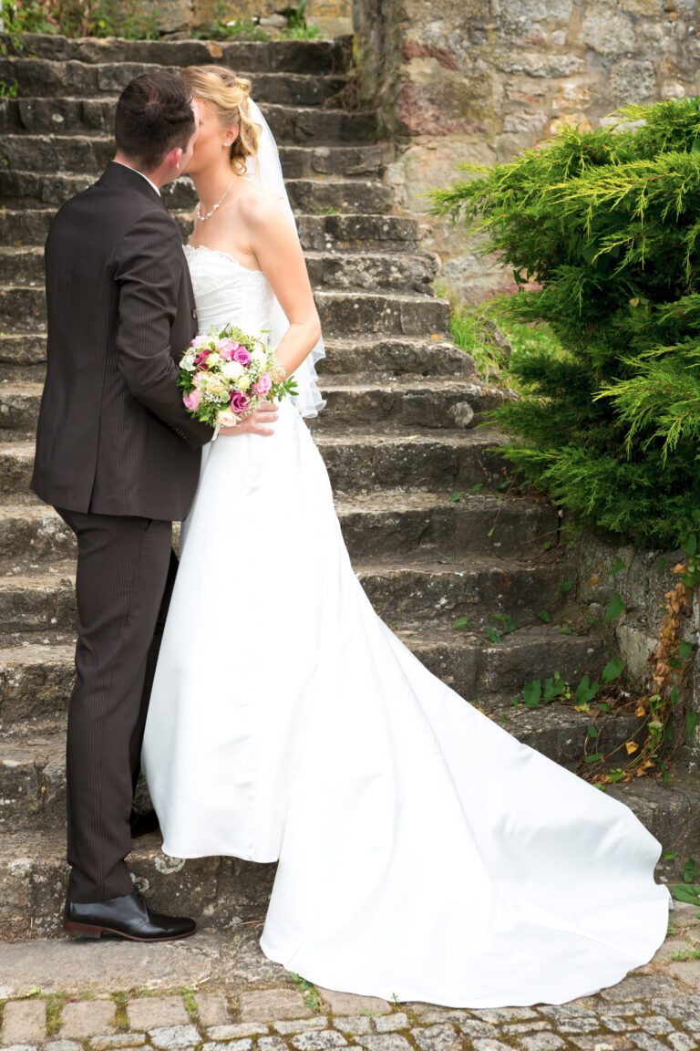 Das Foto zeigt ein junges Ehepaar die auf einer Treppe stehen und sich küssen.