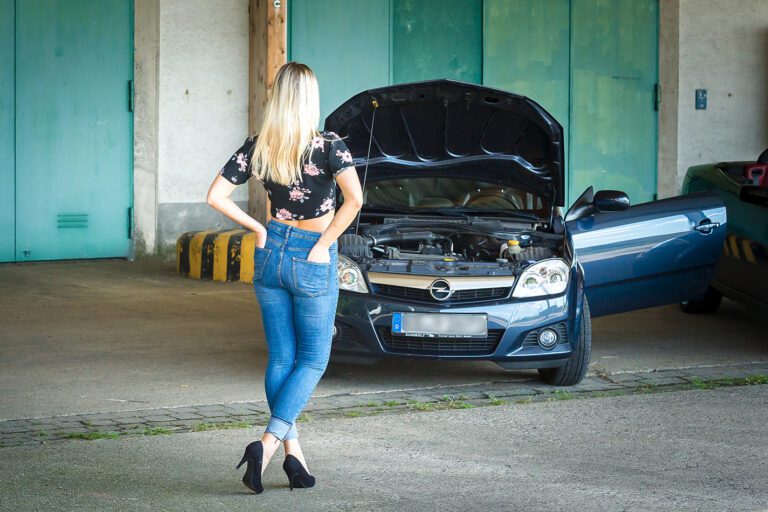 Foto zeigt eine Frau vor einem Auto und einem Gebäude im Sommeroutfit, Bauchfrei und High Heels