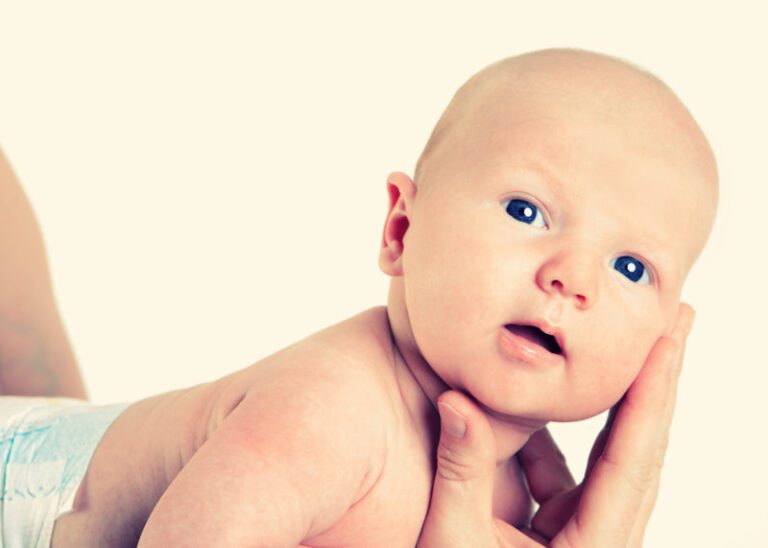 Das Foto zeig ein Baby nur mit Windel an, der Kopf liegt in den Fingern seines Vaters.