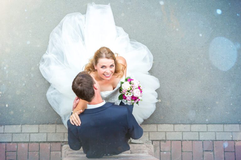 Das Foto zeigt ein junges Ehepaar von oben fotografiert, die Braut schaut in die Kamera er küsst ihre Schulter.