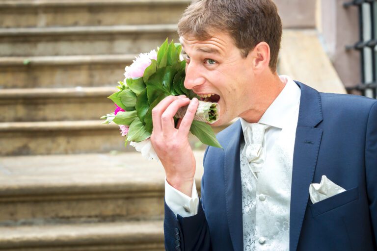 Das Foto zeigt einen jungen Ehemann, der den Brautstrauß seiner Frau anbeisen will.