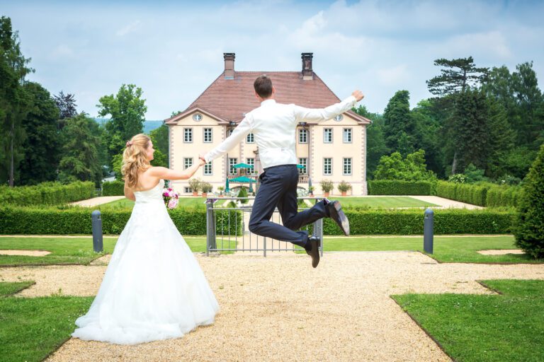 Das Foto zeigt ein junges Ehepaar, er springt vor Glück in die Luft. Beide sind von hinten zu sehen.